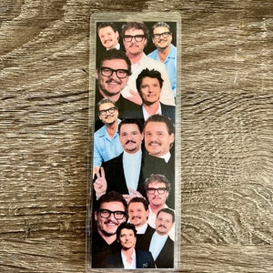 May include: A clear plastic bookmark with a collage of photos of a man with brown hair and a beard. The man is wearing glasses in most of the photos.
