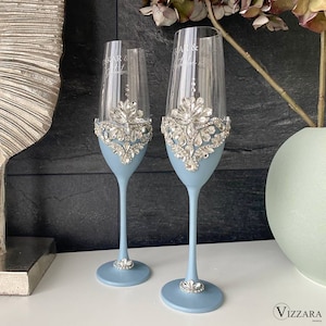 May include: Two light blue champagne flutes with silver rhinestone embellishments. The flutes are decorated with the words "Mr. & Mrs." in a light blue font.