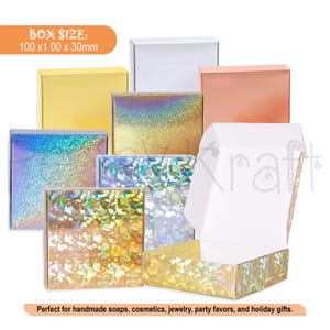 May include: A collection of square cardboard boxes in various finishes including white, solid yellow, metallic rose gold, and holographic patterns. The boxes measure 100 x 100 x 30 mm. One box is shown open, revealing a plain white interior.