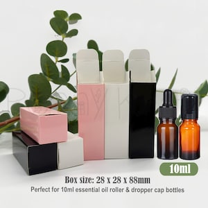 May include: Three rectangular cardboard boxes in pink, white, and black, alongside two amber glass bottles with black caps. One bottle has a dropper, the other a roller ball. Text on the image states: 10ml, Box size: 28 x 28 x 88mm.