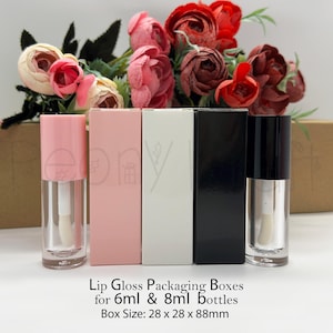 Op de afbeelding: Twee doorzichtige lipgloss-tubes met een roze en een zwarte dop, naast drie rechthoekige verpakkingsdoosjes in roze, wit en zwart. De tekst luidt: Lip Gloss Packaging Boxes for 6ml & 8ml bottles. Box Size: 28 x 28 x 88mm.