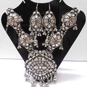 May include: A silver necklace and earrings set with intricate designs and clear stones. The necklace features a large pendant with a circular design and multiple layers of smaller pendants.