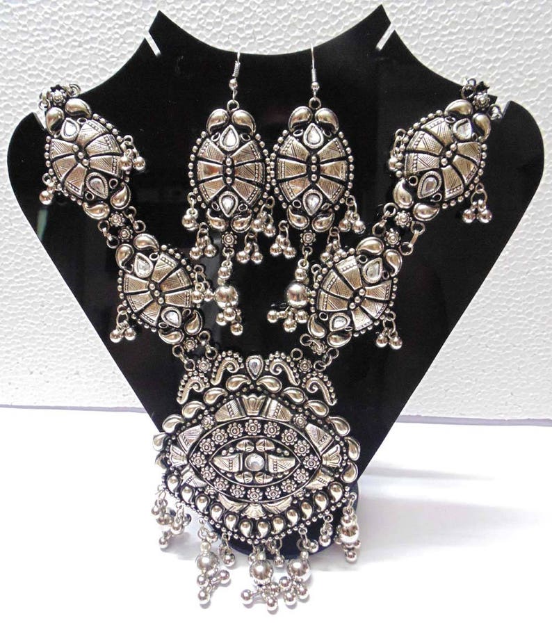 May include: A silver necklace and earrings set with intricate designs and clear stones. The necklace features a large pendant with a circular design and multiple layers of smaller pendants.