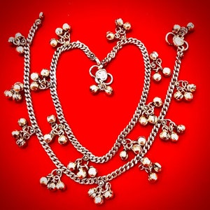 May include: A pair of silver anklets with dangling bells. The anklets are layered and have a delicate chain design.
