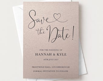 May include: A rectangular save the date card with a shimmering rose gold finish and black text. The card features the script text Save the Date! with a heart icon, followed by the names Hannah & Kyle, the date 18th July 2027, and venue details.