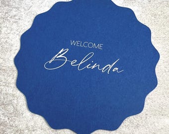 May include: A navy blue, scalloped-edge card with the word "WELCOME" above the name "Belinda" in a cursive font. The card is a solid, deep blue color and is likely used for a special event.