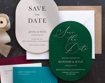 May include: Two oval-shaped save the date cards, one cream with black text and one dark green with white script text. The cream card reads SAVE THE DATE JENNA & PETE 6TH JUNE 2025. The green card reads Save the Date HANNAH & KYLE 18TH JULY 2025.
