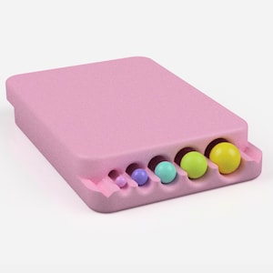 Puede incluir: Un contenedor de pl&aacute;stico rosa con una serie de agujeros en la parte inferior. Cinco bolas de colores son visibles en los agujeros, que van desde el peque&ntilde;o hasta el grande. Las bolas son moradas, azul claro, turquesa, verde claro y amarillas.