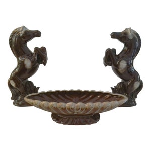 May include: A brown ceramic serving dish with two brown ceramic horse figurines on either side. The dish has a scalloped edge and a raised center.
