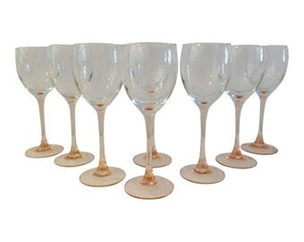 May include: Set of eight clear glass wine glasses with a pink rim. The glasses are arranged in a row on a white background.