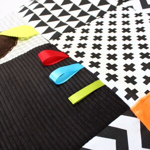 Puede incluir: Una manta sensorial para beb&eacute;s con varios patrones y texturas. Incluye pana negra, tela blanca con cruces y tri&aacute;ngulos negros, y cintas de colores rojo, azul y verde. Incluye una esquina de felpa naranja suave y un borde festoneado amarillo.