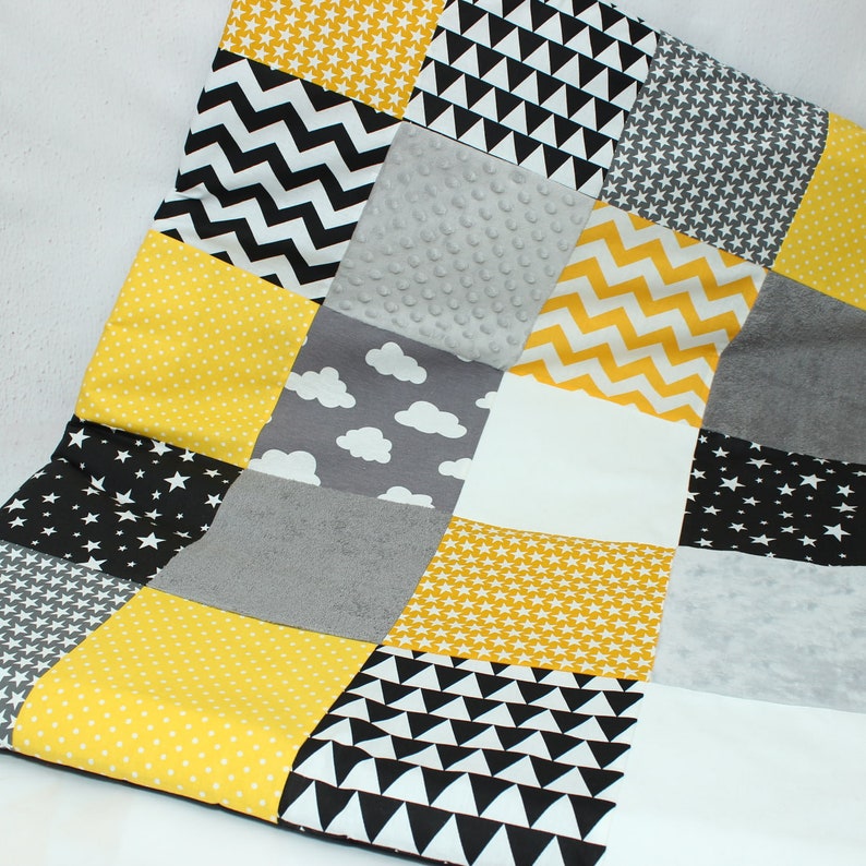 May include: A patchwork quilt featuring a variety of patterns and textures. The quilt incorporates yellow, black, white, and gray fabrics with star, chevron, cloud, and polka dot designs. The quilt is a mix of soft and textured materials.