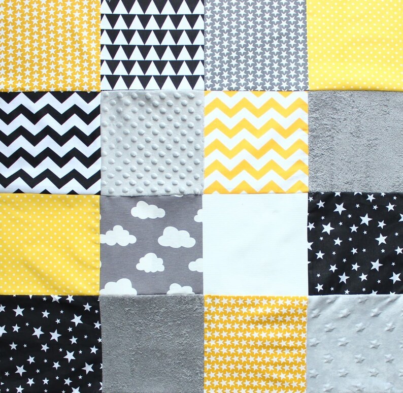 May include: A patchwork quilt featuring a variety of fabrics in yellow, gray, black, and white. Patterns include stars, chevrons, triangles, polka dots, and clouds. Some squares have textured surfaces.