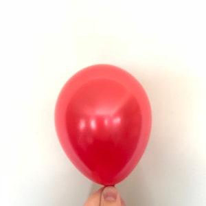 Może przedstawiać: Jeden czerwony balon trzymany przez rękę.