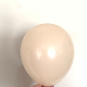 May include: A single, off-white balloon, inflated and held by a hand.
