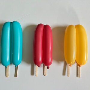May include: Three balloon popsicles, one blue, one red, and one yellow, with wooden sticks.