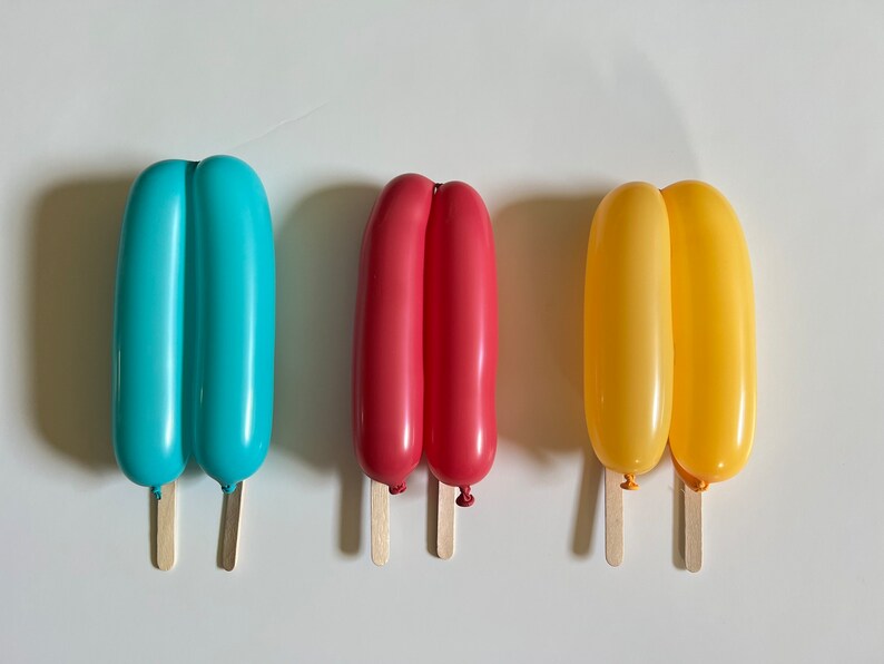 May include: Three balloon popsicles, one blue, one red, and one yellow, with wooden sticks.