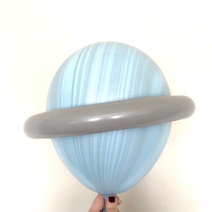 May include: A light blue balloon with a gray ring around it, resembling a planet with rings. The balloon is held by a hand.