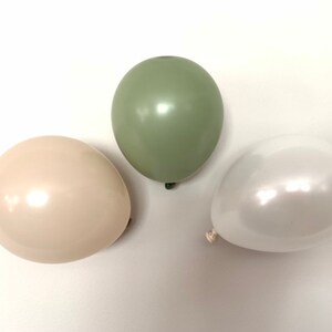 May include: Three latex balloons in different colors: sage green, cream, and white. The balloons are shiny and have a pearlescent finish.