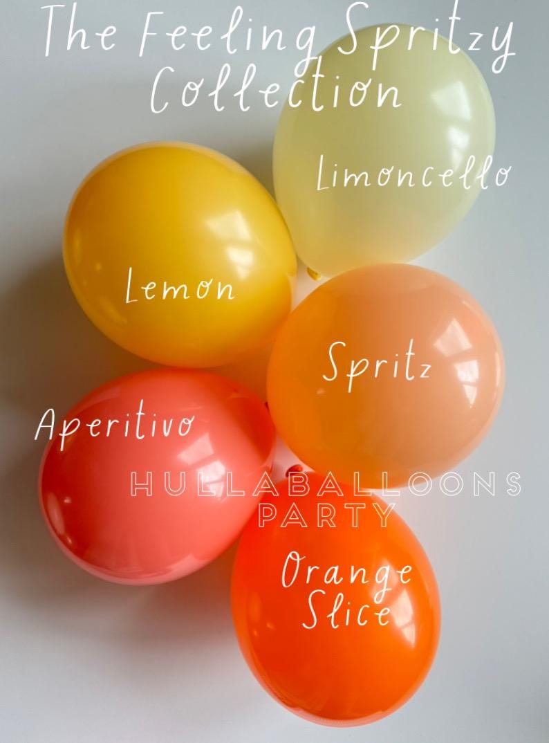 Op de afbeelding: Een verzameling kleurrijke ballonnen in geel, oranje en rood. Elke ballon heeft een smaaknaam erop: Citroen, Limoncello, Spritz, Aperitivo en Sinaasappelschijf. De tekst "The Feeling Spritzy Collection" staat bovenaan.