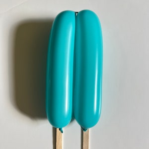 May include: Two blue balloons tied together with a string and attached to wooden sticks, resembling a popsicle.