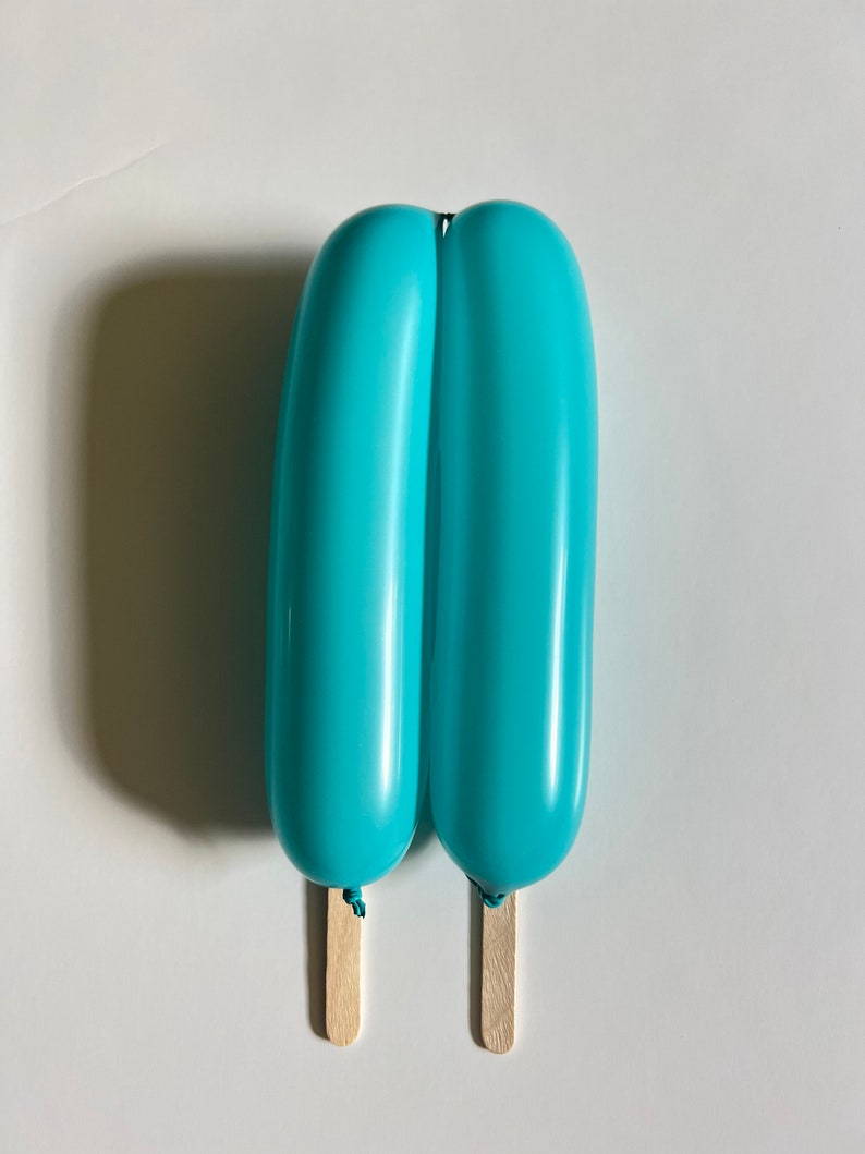 May include: Two blue balloons tied together with a string and attached to wooden sticks, resembling a popsicle.