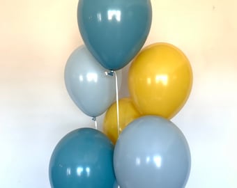 Könnte beinhalten: Ein Bund aus sechs Ballons in Blau- und Gelbtönen. Die Ballons sind mit weißen Bändern zusammengebunden. Die Ballons sind in verschiedenen Blautönen gehalten, darunter ein dunkleres Türkis und ein helleres Graublau, mit zwei gelben Ballons.