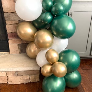 May include: A garland of green, gold, and white balloons. The balloons are arranged in a cascading pattern, with the green balloons at the top and the white balloons at the bottom. The gold balloons are interspersed throughout the garland.