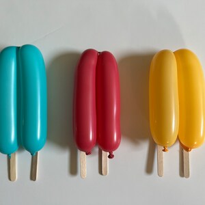 May include: Three balloon popsicles on wooden sticks. The popsicles are blue, red, and yellow.