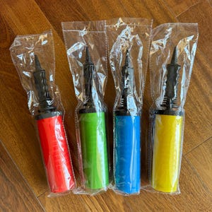 May include: Four colorful hand air pumps in clear plastic packaging. The pumps are red, green, blue, and yellow, each with a black nozzle and handle. The pumps are cylindrical and appear to be made of plastic.