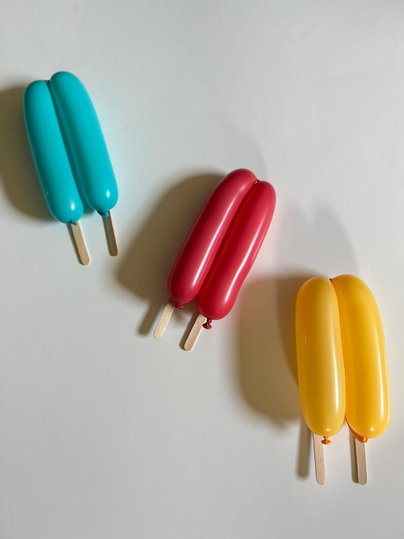 May include: Three balloon popsicles on sticks. The popsicles are blue, red, and yellow.