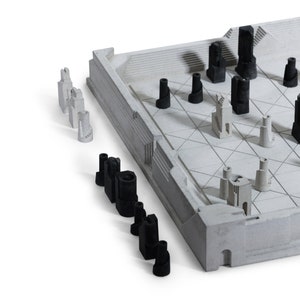 May include: A modern chess set with a concrete-like board and architectural-style pieces. The pieces are in black and white, resembling miniature buildings. The board has a geometric design, and the set is on a white background.