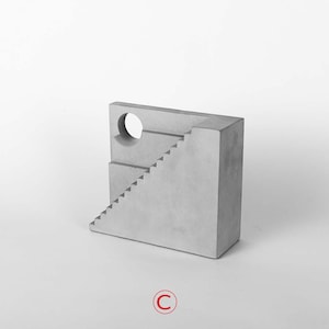 Puede incluir: Una escultura de hormig&oacute;n gris de un edificio con una escalera y una abertura circular. La escultura est&aacute; sobre un fondo blanco.