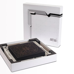 May include: A black box with an intricate gold design sits inside a white box. The white box has a geometric design and the word "ARENA" printed on it. The box is open, revealing the contents.