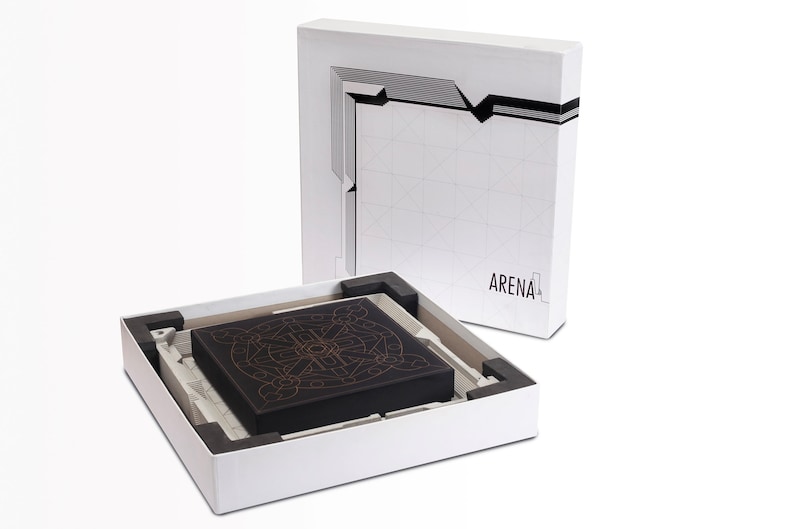May include: A black box with an intricate gold design sits inside a white box. The white box has a geometric design and the word "ARENA" printed on it. The box is open, revealing the contents.