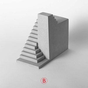 Puede incluir: Una escultura de hormig&oacute;n gris con una escalera y un bloque rectangular. La escultura est&aacute; sobre un fondo blanco.