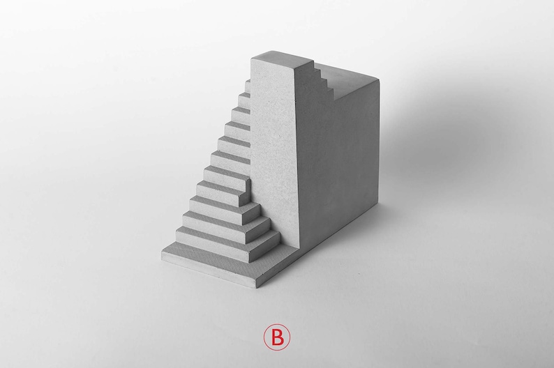 Puede incluir: Una escultura de hormig&oacute;n gris con una escalera y un bloque rectangular. La escultura est&aacute; sobre un fondo blanco.
