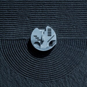 May include: A gray, abstract, geometric design on a black, textured surface. The design resembles a building with multiple levels and windows.