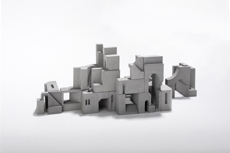 May include: A model of a small city made of gray concrete blocks. The blocks are stacked on top of each other in a random pattern, creating a variety of shapes and sizes. The model is set against a white background.