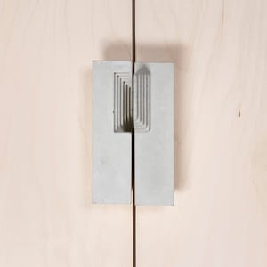 Può includere: Una coppia di maniglie per porte in cemento con un design geometrico. Le maniglie sono fissate a una superficie in legno chiaro.