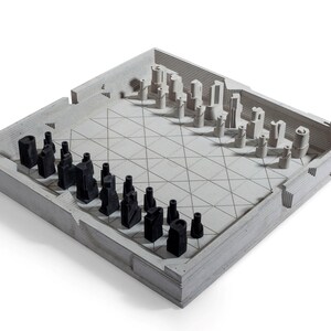 May include: A modern chess set with a concrete board and pieces. The board is light gray with a grid pattern, and the pieces are black and light gray. The pieces have a unique, architectural design. The set is displayed on a white background.