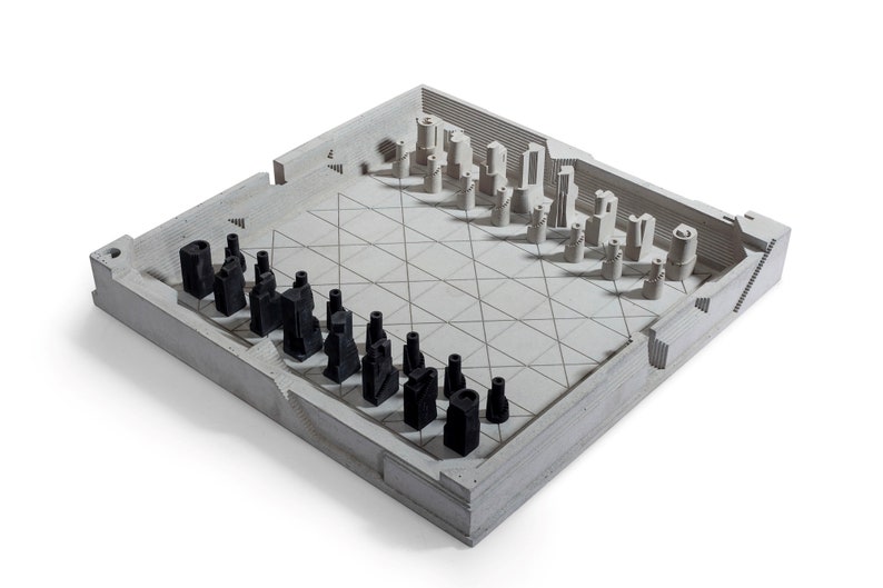 May include: A modern chess set with a concrete board and pieces. The board is light gray with a grid pattern, and the pieces are black and light gray. The pieces have a unique, architectural design. The set is displayed on a white background.