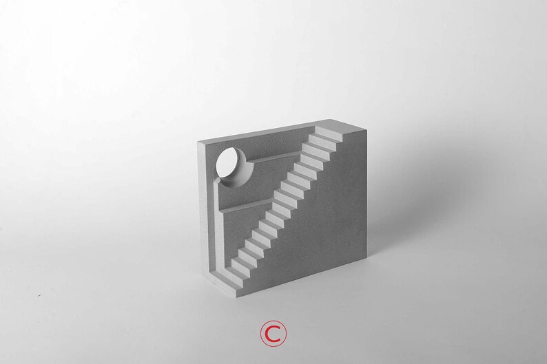 Puede incluir: Una escultura de hormig&oacute;n gris de un edificio con una escalera y una abertura circular. La escultura est&aacute; sobre un fondo blanco.