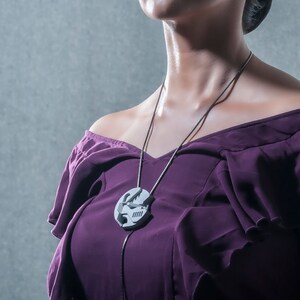 May include: A woman wearing a purple off-the-shoulder dress with a silver chain necklace featuring a geometric pendant.