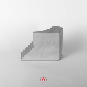 Puede incluir: Una escultura de hormig&oacute;n gris de una escalera con una esquina, sobre un fondo blanco.