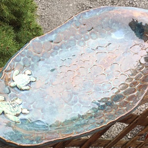 May include: A light blue ceramic serving dish with a textured surface and two white turtle figurines. The dish is oval shaped and has a rustic, handmade look.