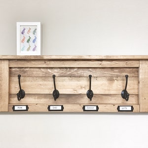 May include: Rustic wooden coat rack with four hooks and a shelf. The hooks are labeled "Mom", "Dad", "Johnny", and "Kate".