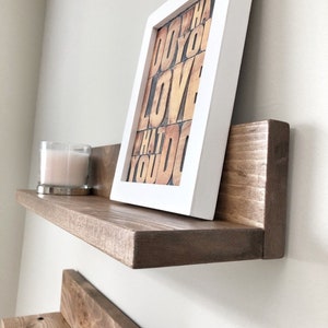 May include: A floating wooden shelf with a framed print that reads "DO WHAT YOU LOVE WHAT YOU DO." A lit candle in a glass holder sits on the shelf. The frame is white, and the shelf is stained brown.