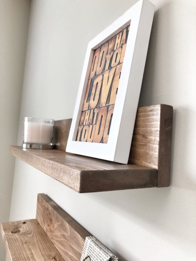 May include: A floating wooden shelf with a framed print that reads "DO WHAT YOU LOVE WHAT YOU DO." A lit candle in a glass holder sits on the shelf. The frame is white, and the shelf is stained brown.