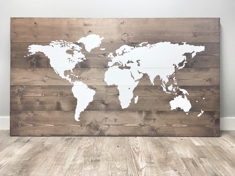 Pode incluir: Um mapa mundial pintado de branco sobre um fundo de madeira marrom. O mapa &eacute; delineado em branco e est&aacute; centralizado no painel de madeira.